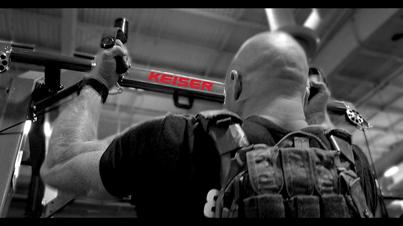 Black and white image of a tactical athlete using a Keiser rack for weighted pullups. 