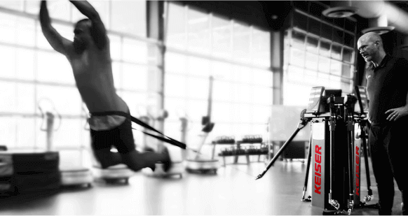 Black and white image. of an athlete jumping forward while attached to the Functional Trainer