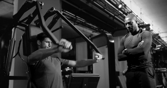 Black and white image of an athlete using the Keiser chest press while his trainer observes.