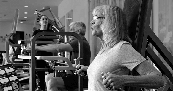 Black and white image of an older adult working out on the triceps machine